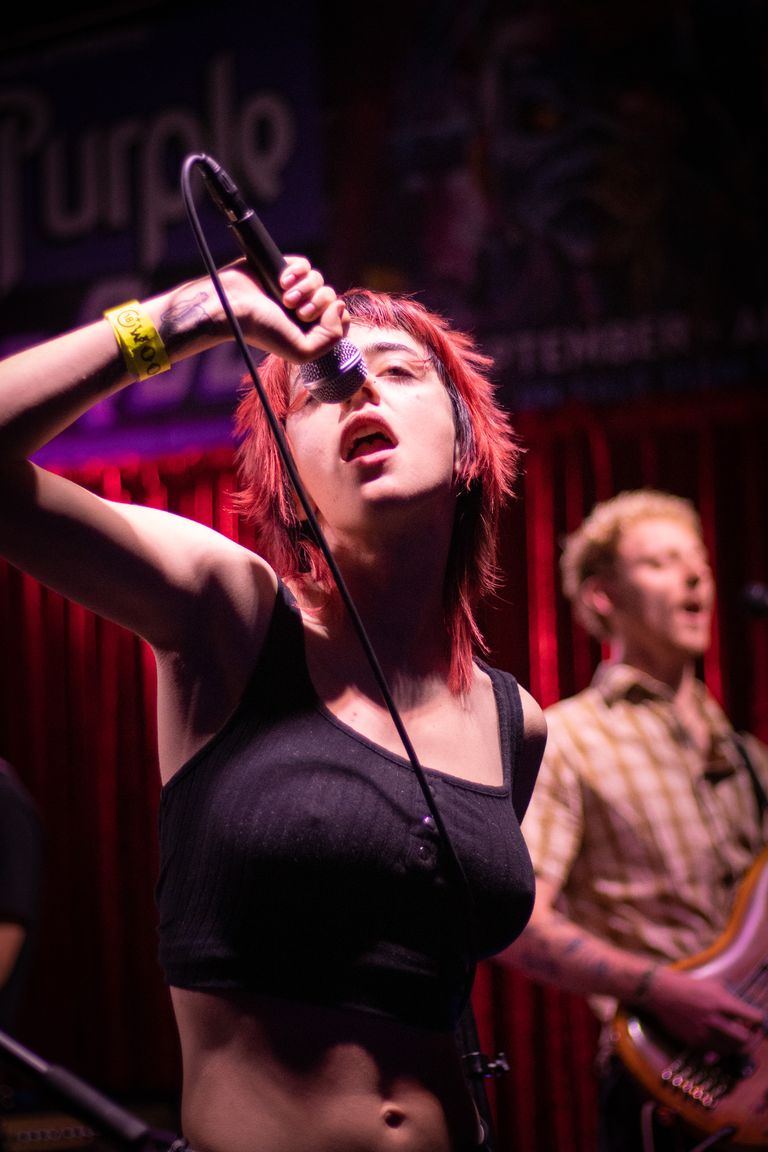 South Australian singer with short red hair singing into a microphone on stage with a red velvet backdrop during a live venue performance.